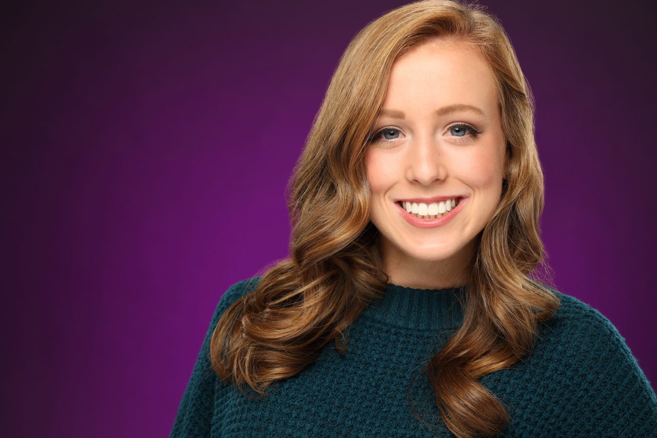 Exulting Images dancer headshot of young woman with blue eyes and curled brown hair against a purple background