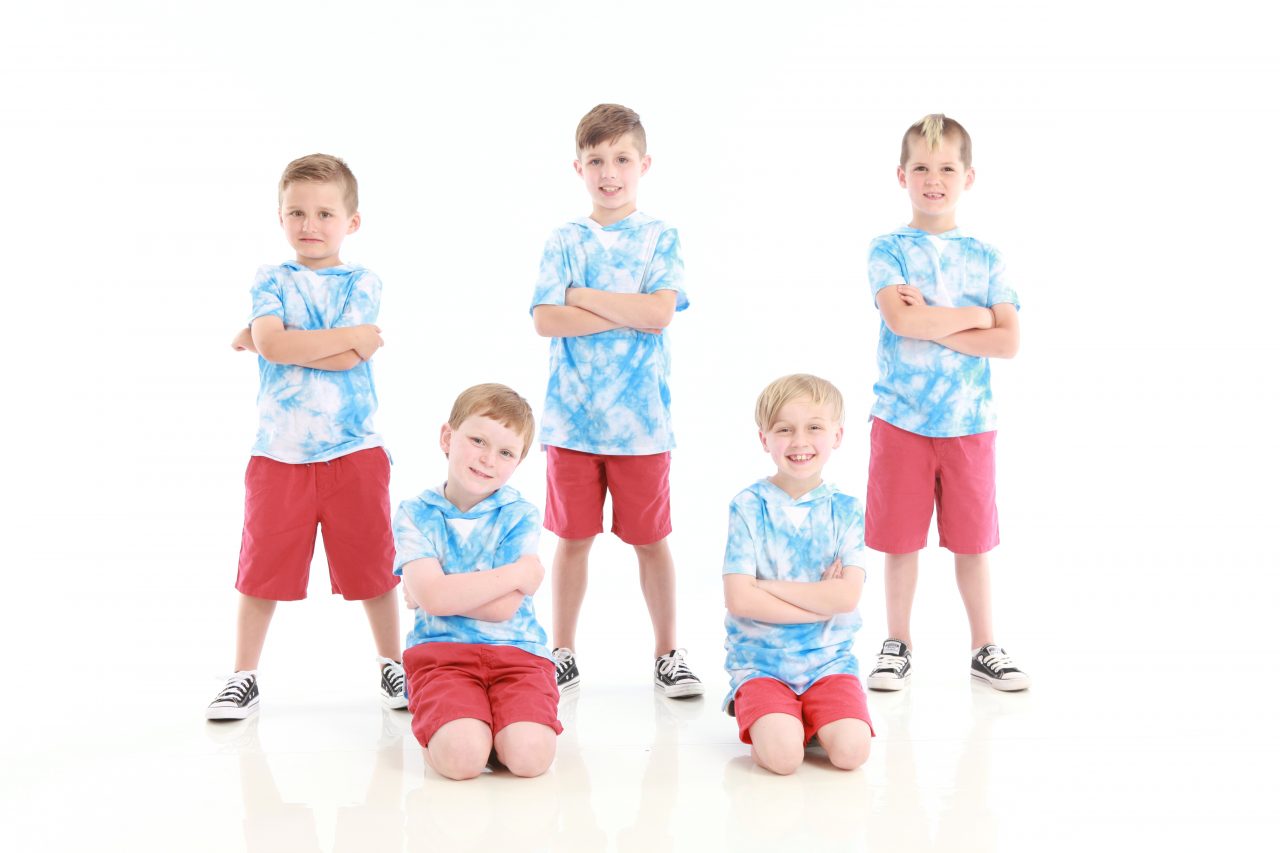 Five young male dancers wearing light blue tie-dye shirts and red shorts pose with arms crossed for dance recital photography in Exulting Images’ Fort Mill SC studio