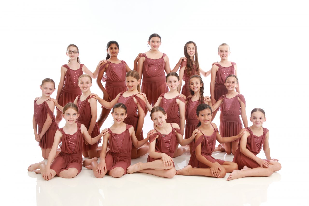 Group of young pre-teen dancers wearing terra cotta colored dance costumes pose for dance recital photography in Exulting Images’ Fort Mill SC studio