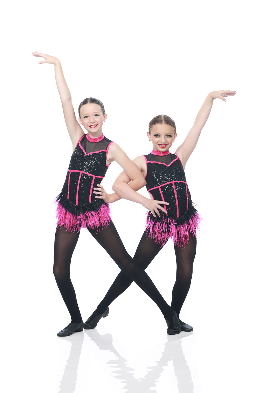 Two young female dancers in black and pink costumes with feathered trip pose for dance recital photography in Exulting Images’ Fort Mill SC studio