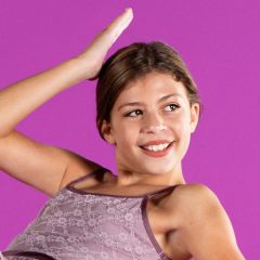 Young girl looking slightly off to the side smiles and poses in purple costume for professional headshot photographer Exulting Images in their Fort Mill, SC studio