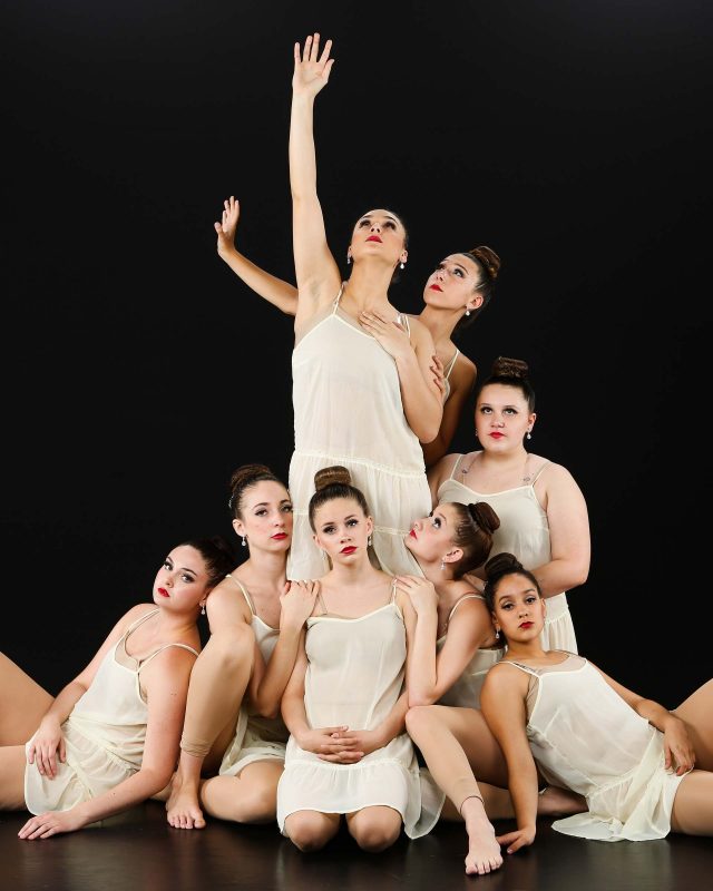 Eight young female dancers in white smocks pose for Exulting Images’ dance recital photography