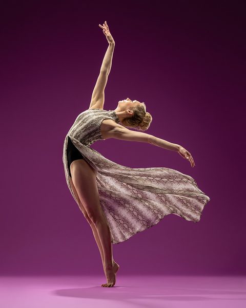 Dance action shot of female dancer in flowing dress on tip toe leaning back with arms spread gracefully in Exulting Images’ Fort Mill, SC dance photography studio