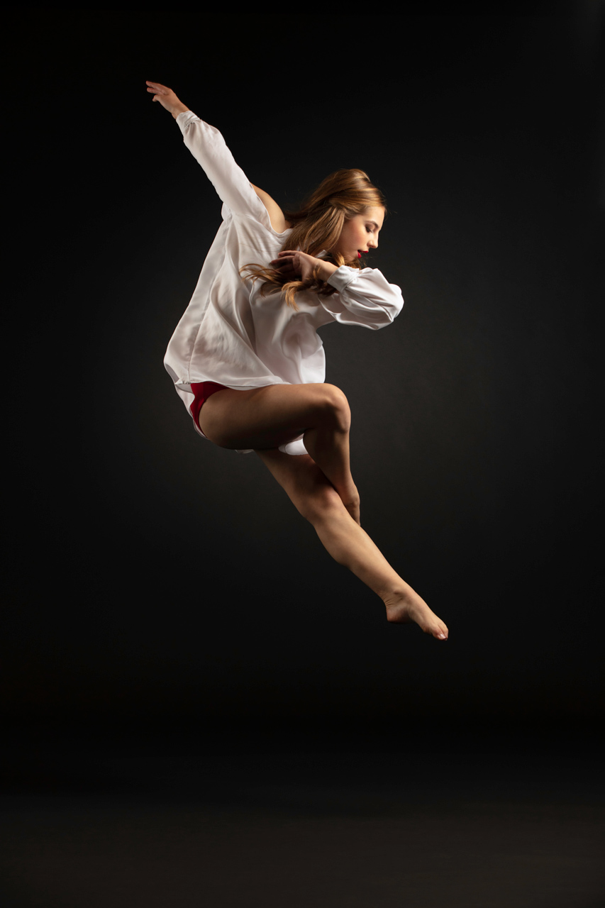 Dramatically shadowed professional dance portrait captured mid air of dancer wearing white smock with toes pointed