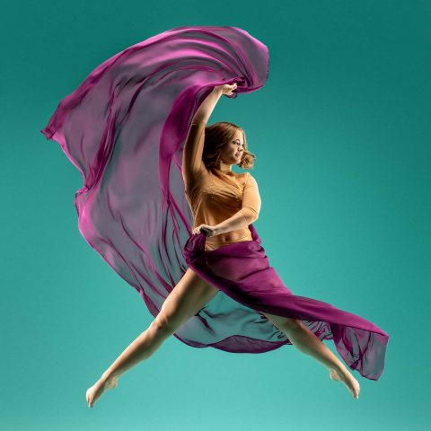 Modern dance action shot of female dancer wearing beige stretching sheer wine colored fabric behind her on a teal background in Exulting Images' Fort Mill, SC studio