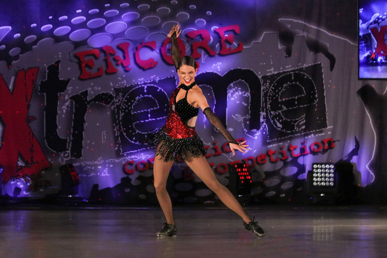 Smiling female tap dancer wearing black and red costume onstage during dance competition photographed by Exulting Images