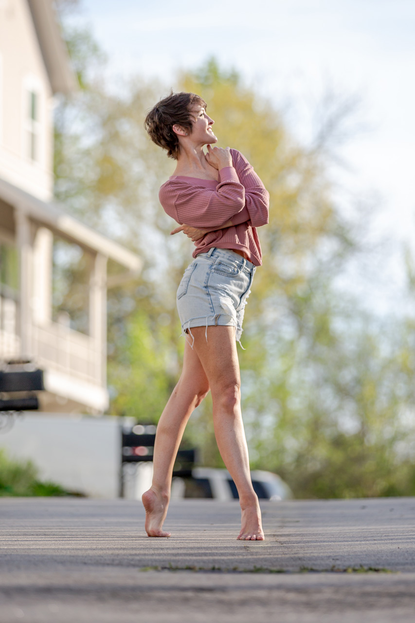 Outdoor dance portrait by Exulting Images of short haired female in light wash denim shorts and mauve top on tiptoe with arms wrapped around herself