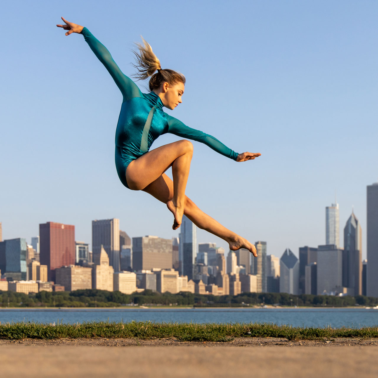 Female dancer in teal captured mid leap with the background of Chicago skyline for Exulting Images outdoor dance photoshoot