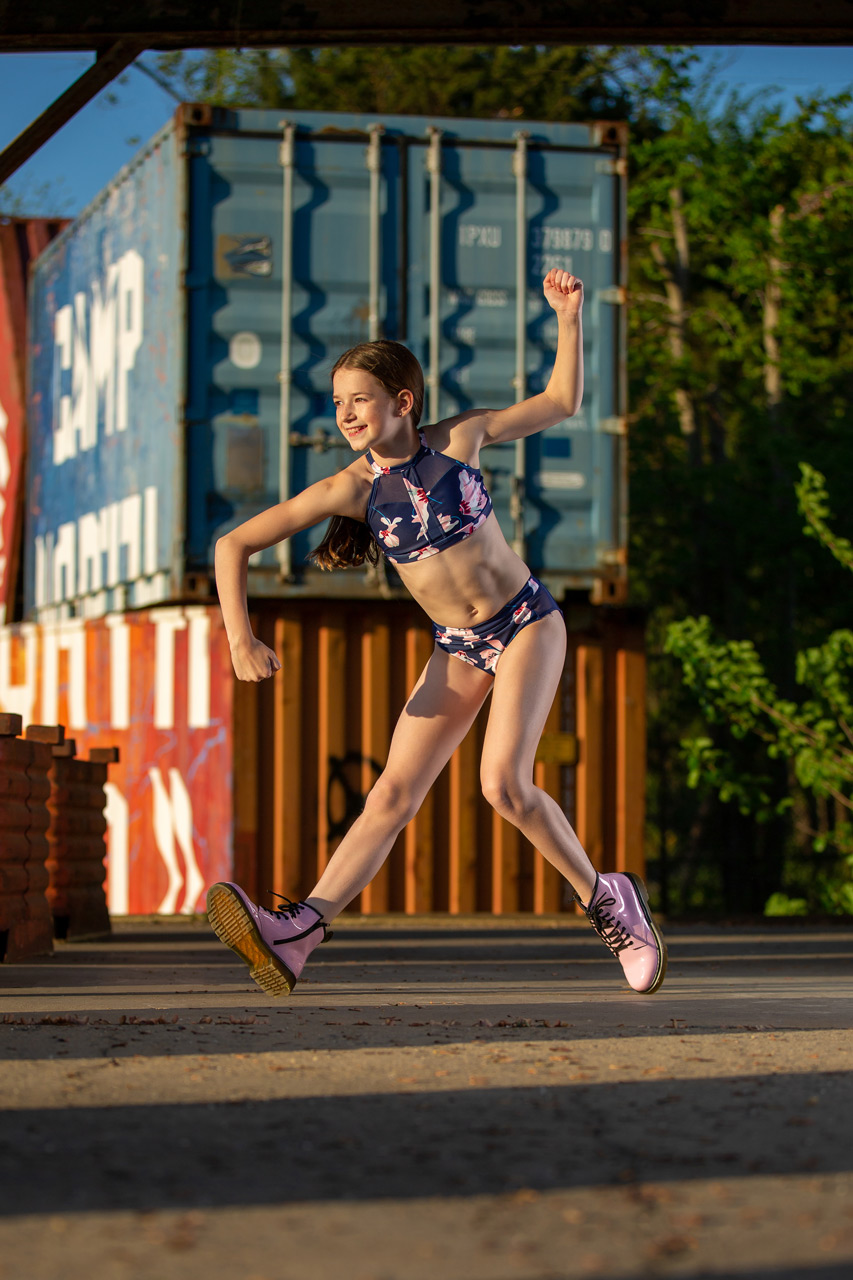 Contemporary outdoor dance action shot of young girl dancing in front of stacked metal shipping containers