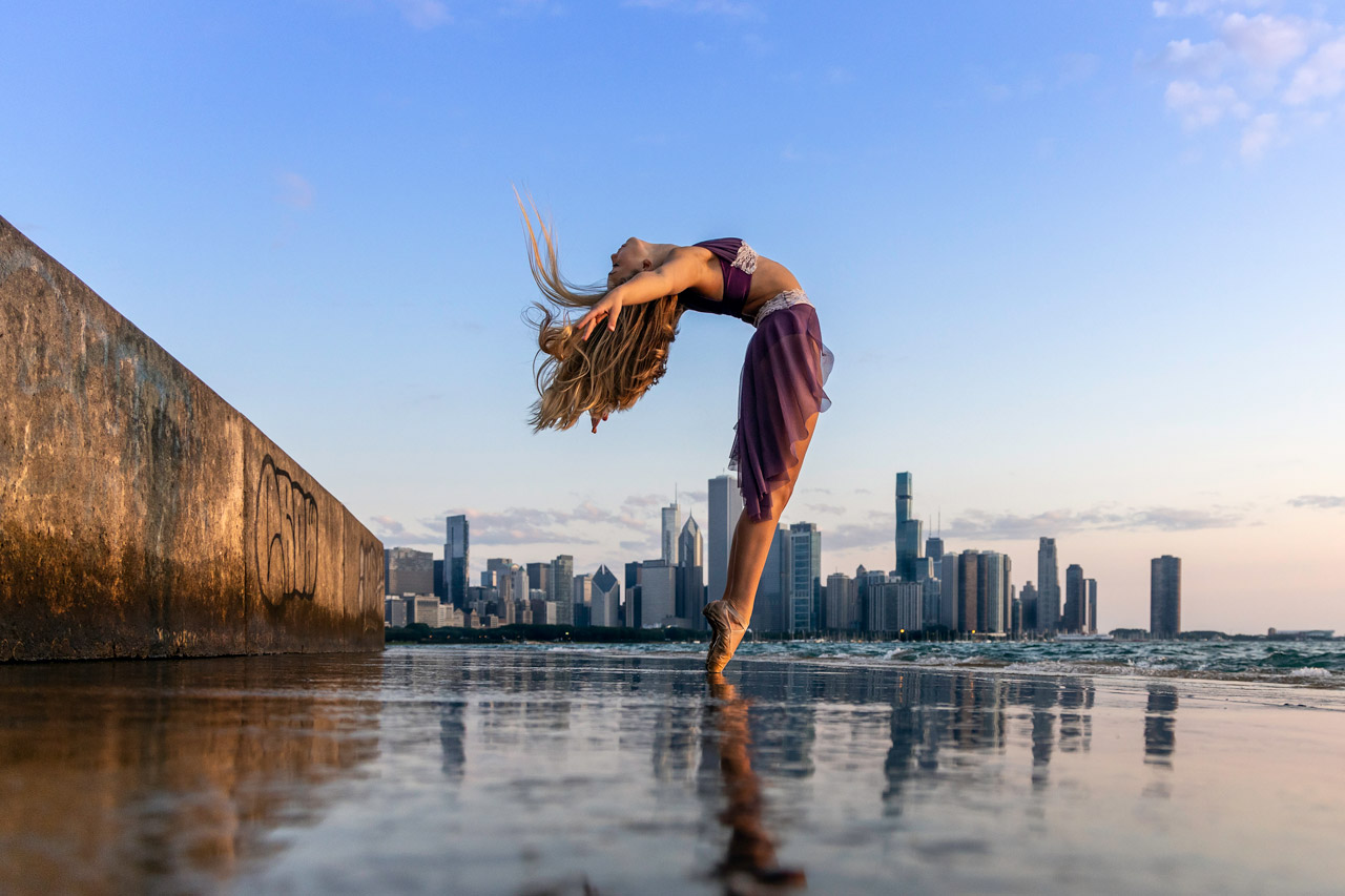 Young blond-haired female dancer gracefully poses for professional outdoor ballet pictures with a portion of the Chicago skyline in the background