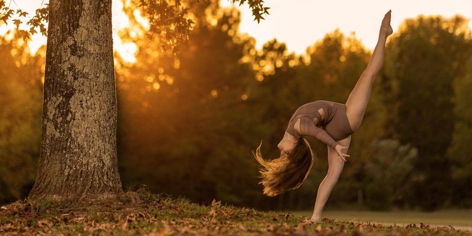 Female in graceful back bend with leg pointed toward the sky during fall dance photoshoot outdoors