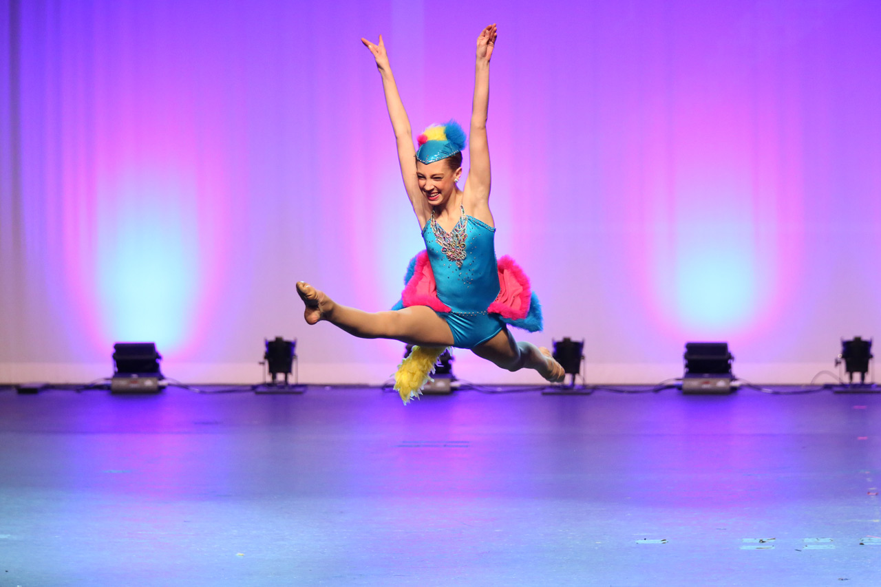 Smiling teenage dancer leaping on stage during dance recital photographed by Exulting Images