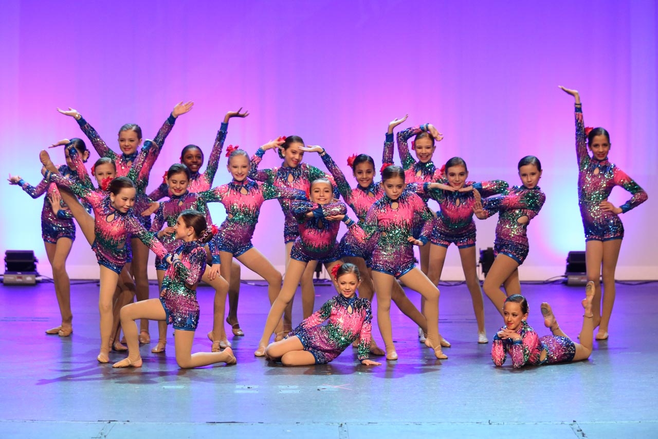 Group of young female dancers in multicolored sequined outfits posing on stage during dance recital photographed by Exulting Images