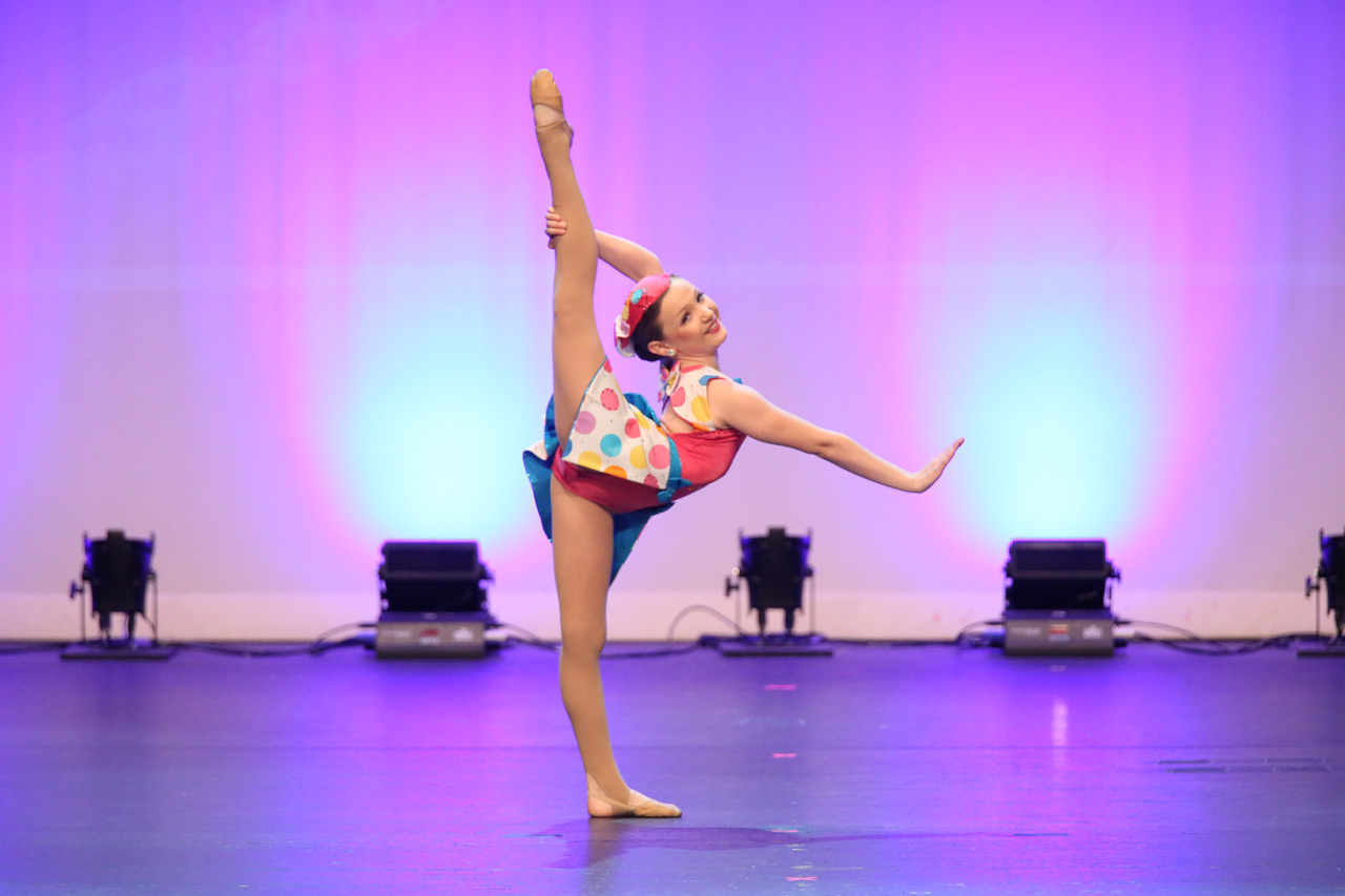 Exulting Images’ dance recital photograph of young female dancer in multicolored polka dot costume holding lifted leg behind her