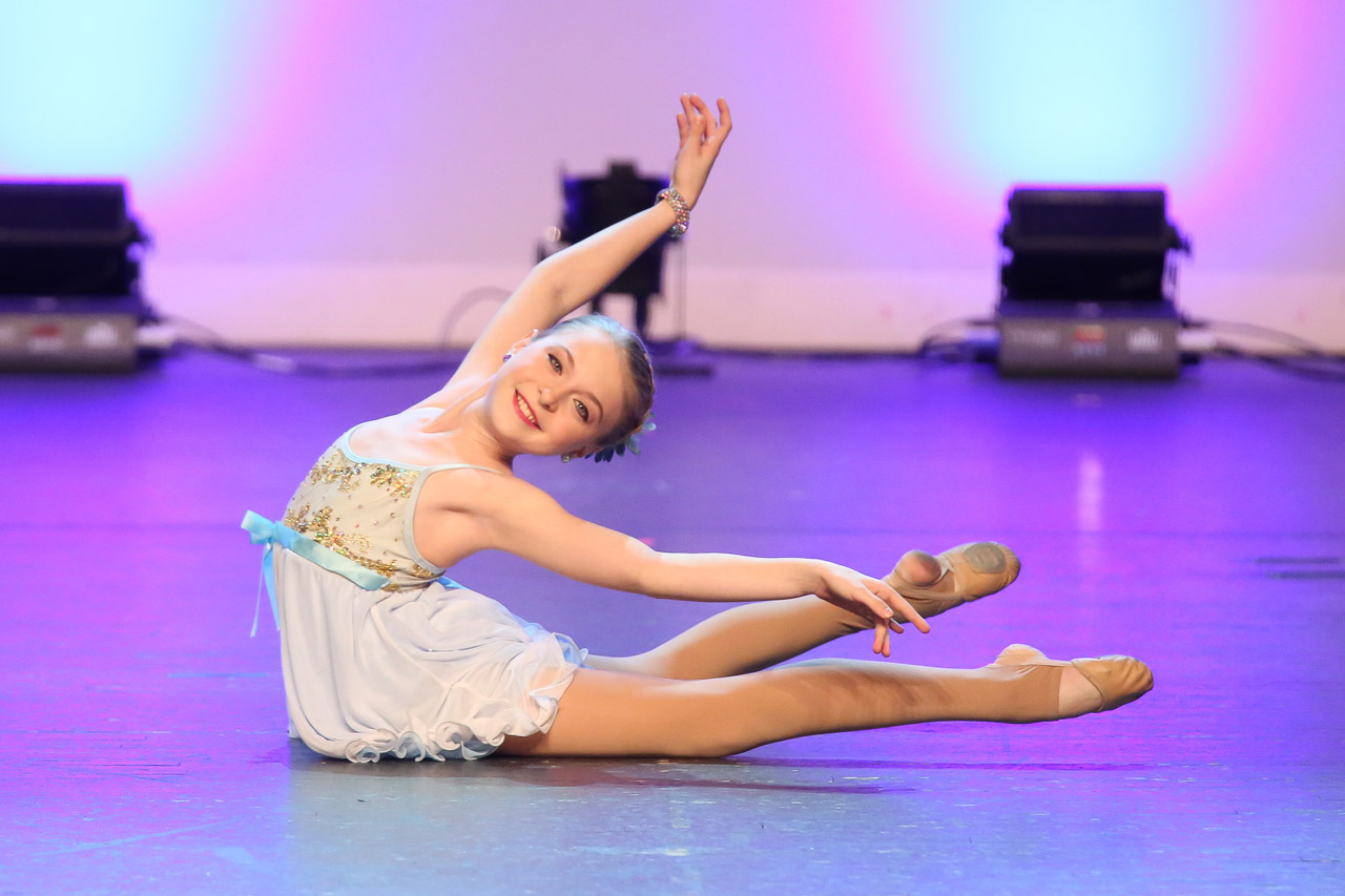 Young female dancer laying with back arched and arms stretched back looking directly at camera in Exulting Images’ dance recital photograph