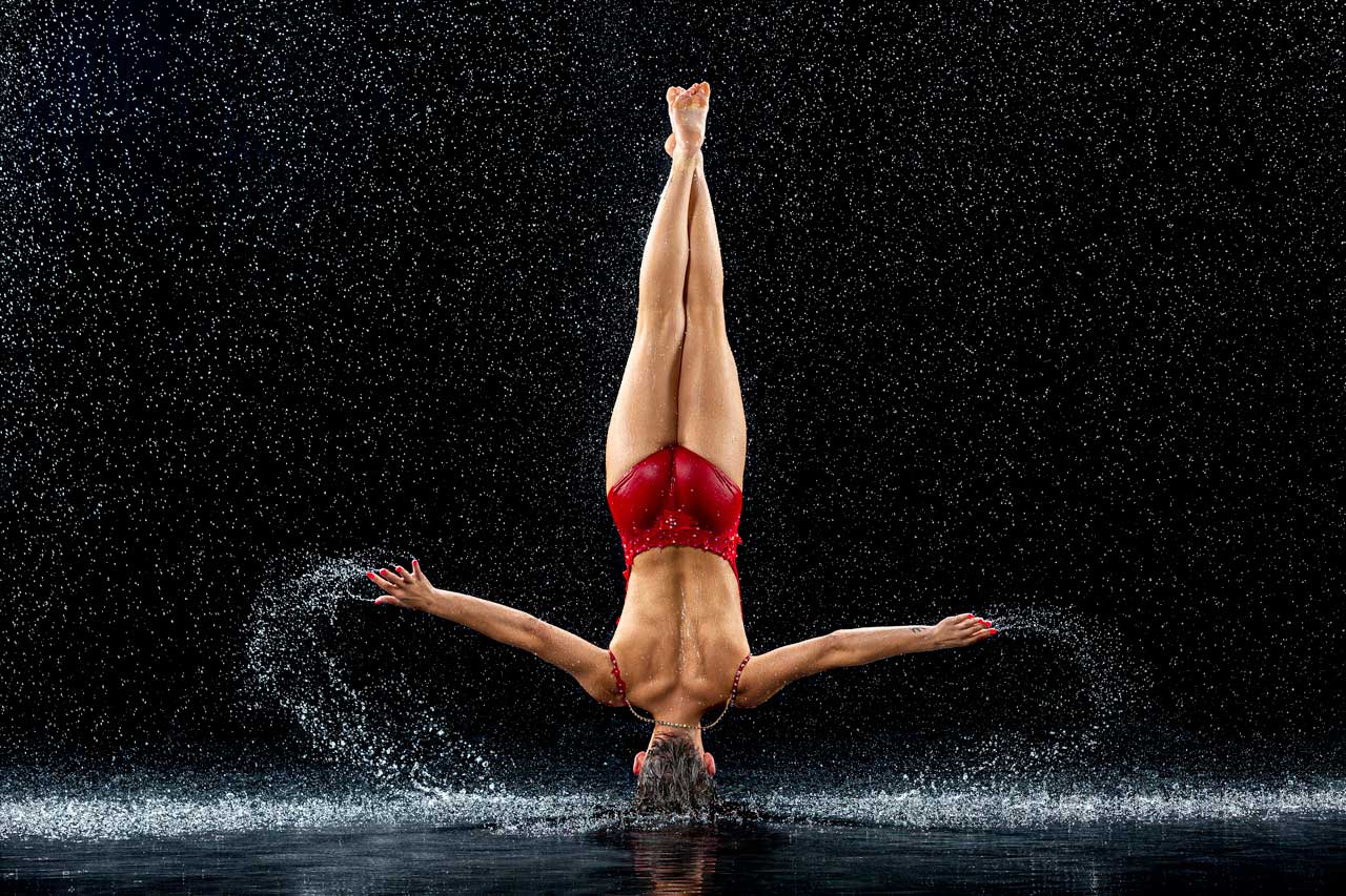 Dancer wearing red poses in a headstand splashing water in Exulting Images’ rain room photoshoot