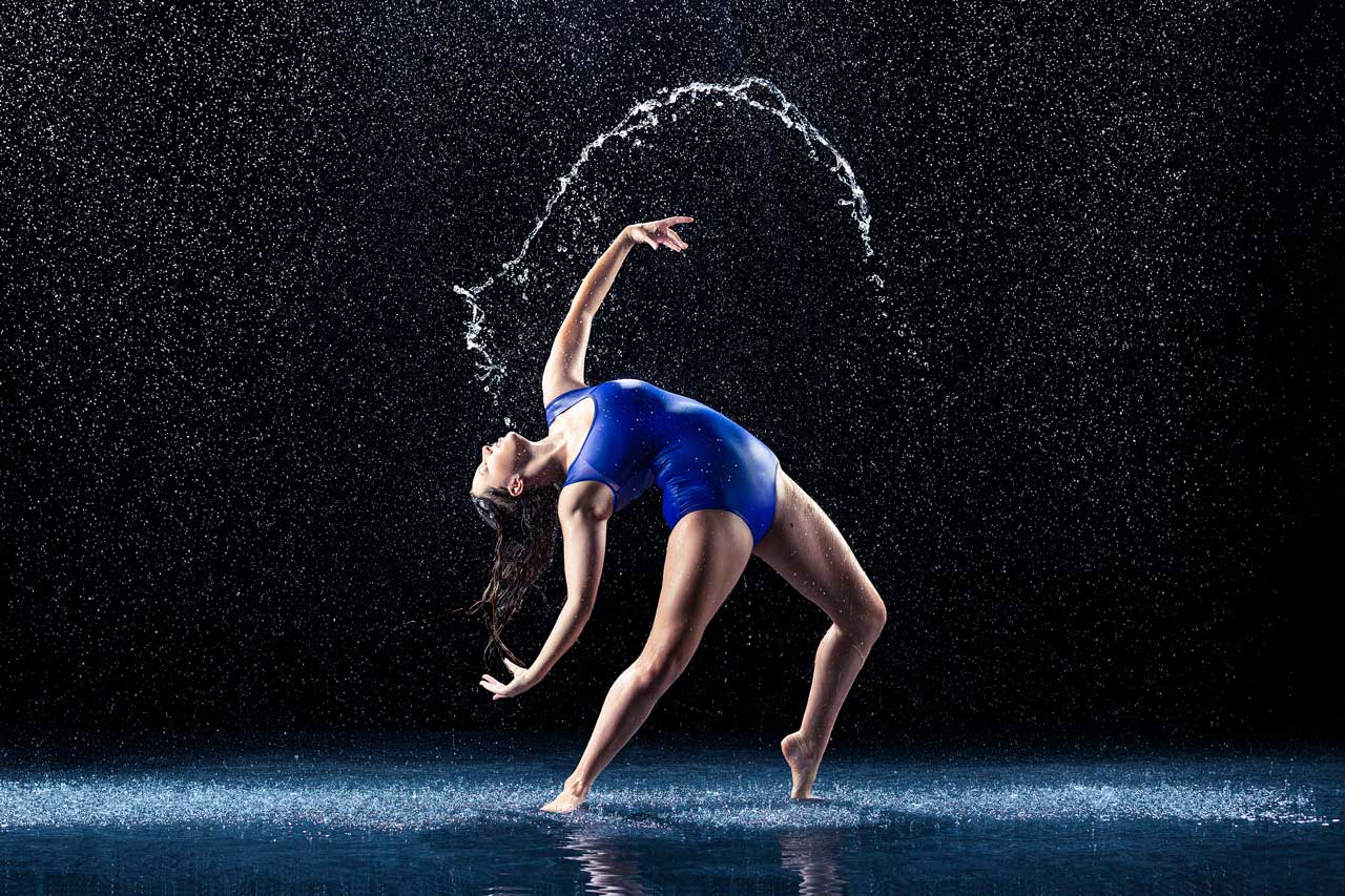 Exulting Images' rain room photoshoot of brunette female dancer wearing a blue leotard in a deep backbend