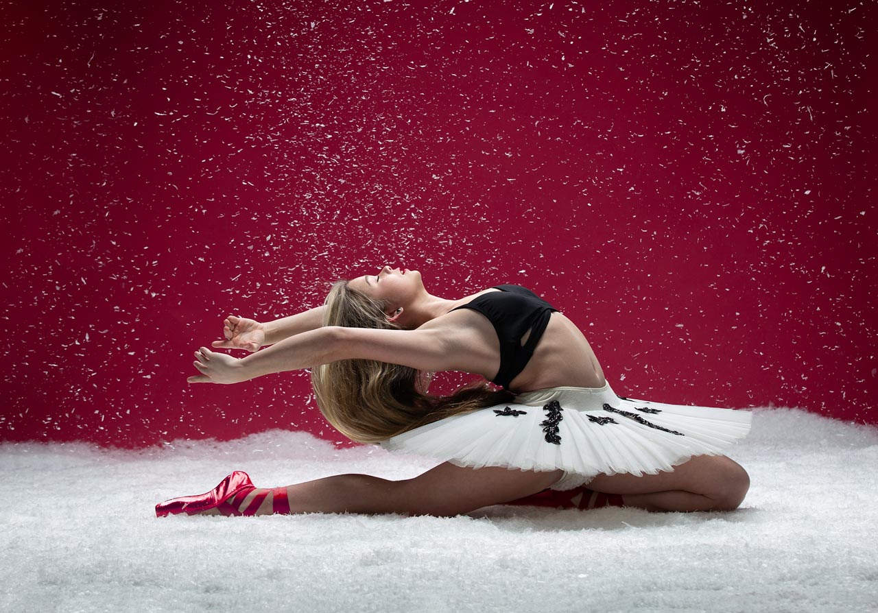 Teenage ballerina in white tutu and red point shoes poses on the snowy ground in a deep backbend for Exulting Images Fort Mill, SC professional dance photography studio