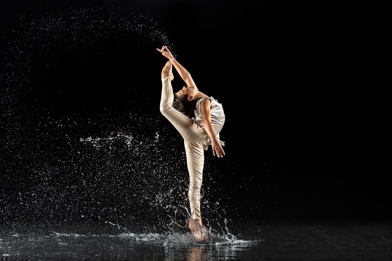 Young male dancer in champagne colored costume with leg raised behind him in a needle pose for Exulting Images dance photography with rain